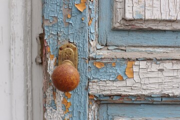 Close view of an old door featuring chipping blue paint and a classic doorknob, showcasing urban decay and history