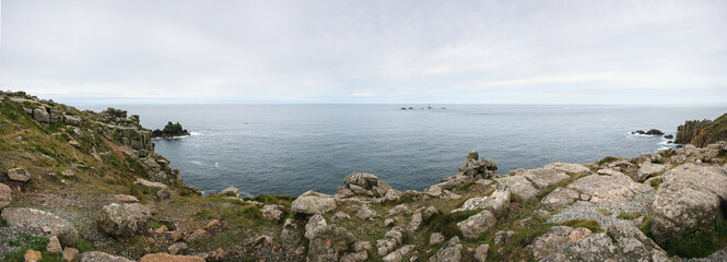 Panorama of Cornwall rocky shoreline, with cliffs near shore, Longships lightouse visible in distance