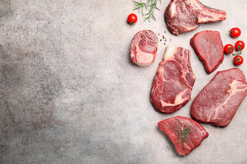 Pieces of raw beef meat, spices and tomatoes on grey table, flat lay. Space for text