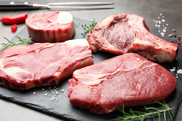 Pieces of raw beef meat, spices and carving fork on grey table, closeup