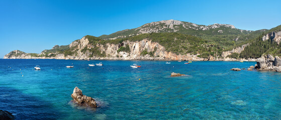 Bay of Liapades with many motorboats, sun shines on clear blue water, trees covered cliffs in background