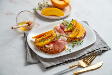 Bruschetta with peach, cream cheese, prosciutto and honey on a plate on a marble background