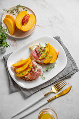 Bruschetta with peach, cream cheese, prosciutto and honey on a plate on a marble background