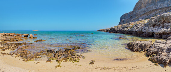Sun shines on wet sand and rocks at Navarone Bay, Rhodes island, nice remote beach