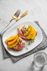 Sandwich with peach, cream cheese, prosciutto and honey on a plate on a marble background