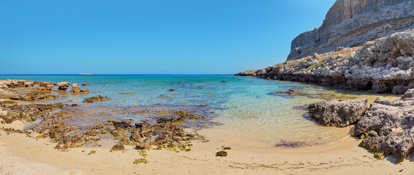 Sun shines on wet sand and rocks at Navarone Bay, Rhodes island, nice remote beach