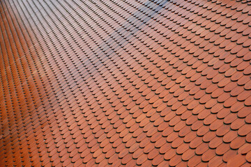Closeup detail to classic red roof tiles arranged in regular pattern, wet from rain