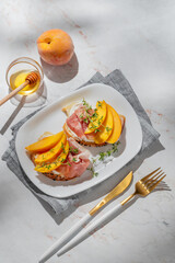 Bruschetta with peach, cream cheese, prosciutto and honey on a plate on a marble background