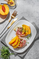 Sandwich with peach, cream cheese, prosciutto and honey on a plate on a gray background