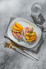 Toast with peach, cream cheese, ham and honey on a plate on a gray background with thyme