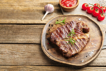 Delicious grilled beef steak with rosemary, spices and products on wooden table, closeup. Space for text