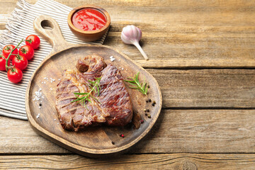 Delicious grilled beef steak with rosemary, spices and products on wooden table, closeup. Space for text
