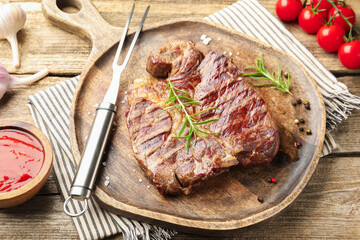 Delicious grilled beef steak with rosemary, spices, carving fork and ketchup on wooden table, closeup