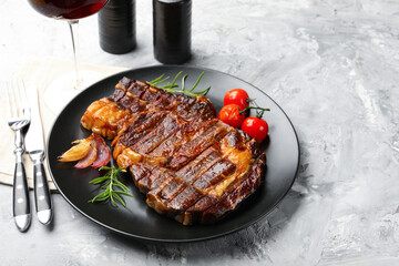 Delicious grilled beef steak with rosemary, onion, tomatoes, cutlery and shakers on grey textured table, closeup. Space for text