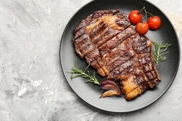 Delicious grilled beef steak with rosemary, onion and tomatoes on grey textured table, top view. Space for text