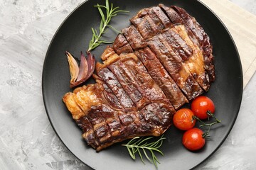 Delicious grilled beef steak with rosemary, onion and tomatoes on grey textured table, top view
