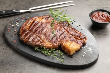 Delicious grilled beef steak with herbs, spices and ketchup on grey textured table, closeup