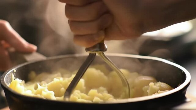 Mashed potatoes being prepared with a potato masher steaming pot