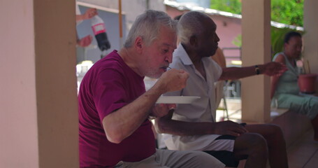 Elderly men conversing on outdoor patio while holding plates of food, relaxed gathering, social...