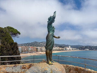 Sculpture of "Doña Marinera," one of the most representative symbols of Lloret de Mar. The bronze statue stands on a rock overlooking the Mediterranean Sea, with the beach and mountains. Spain