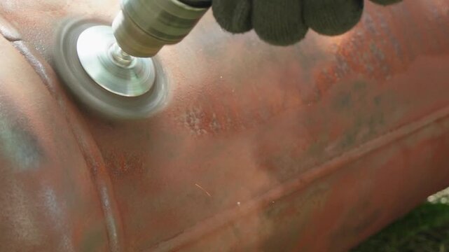 Electric drill with wire brush attachment polishing rusty metal surface close-up