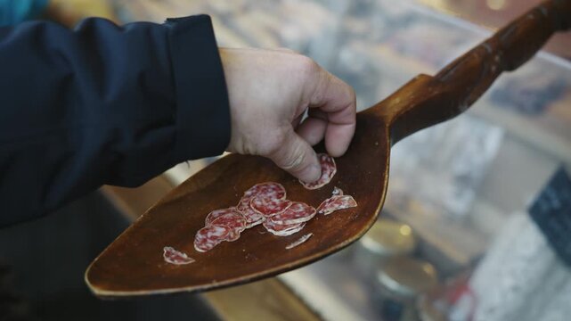 A wooden spoon with a pile of tasters pepperoni slices on it at Christmas market in Germany. The spoon is on display in a store