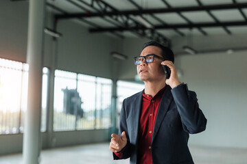 Asian businessman making phone call, discussing a deal or property in an empty commercial space. Real estate and business concepts