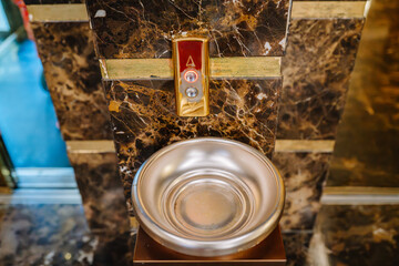 A luxurious hotel elevator call button with an ornate gold and marble design, featuring a decorative silver bowl likely for aesthetic or ceremonial use.