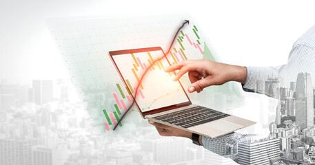 A business professional interacts with a laptop displaying financial data and trends against an...