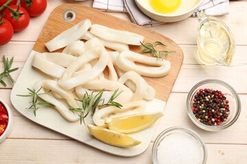Uncooked squid rings, spices, yolk and tomatoes on wooden table, flat lay