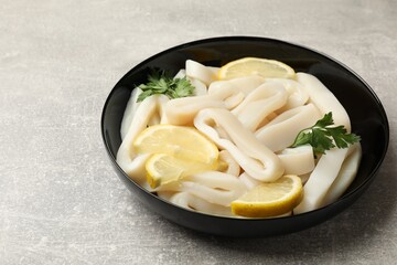 Raw squid rings, lemon and parsley in bowl on grey textured table, closeup. Space for text