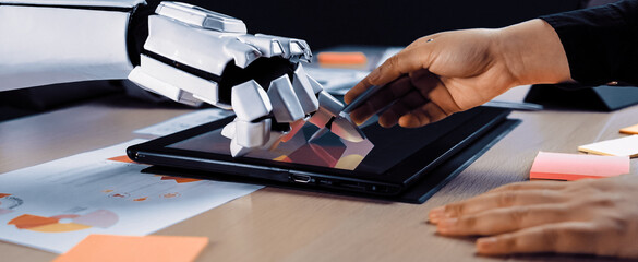 A creative workspace showing a robotic arm and human hand interacting with a touchscreen device, highlighting human-robot collaboration in design and innovation processes.Noogenesis