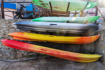 Colorful kayaks stacked on stone wall, vibrant red, yellow, orange, green, and gray boats stored outdoors in bright sunlight.