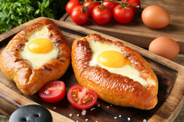 Tasty khachapuris with cheese, eggs and tomatoes on wooden table, closeup