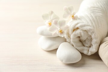 Towel, spa stones and orchid flowers on white wooden table, closeup. Space for text