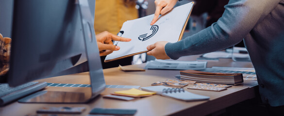A dynamic workspace showcases team members exchanging ideas over a sketch on a clipboard, with a digital screen in a collaborative office setting. SACTR