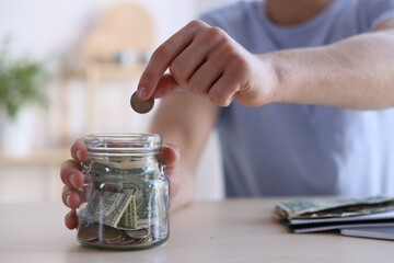 Man putting money into jar at wooden table indoors, closeup