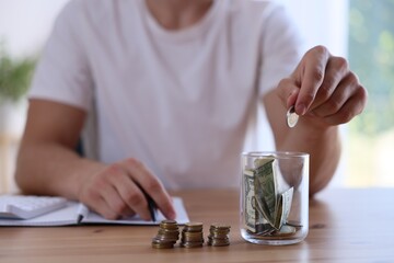 Man putting money into jar at wooden table indoors, closeup
