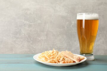 Dried squid snacks and glass of beer on light blue wooden table against grey background, closeup. Space for text