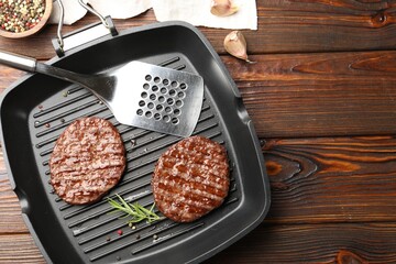 Pan with grilled patties, spices and slotted spatula on wooden table, flat lay. Space for text