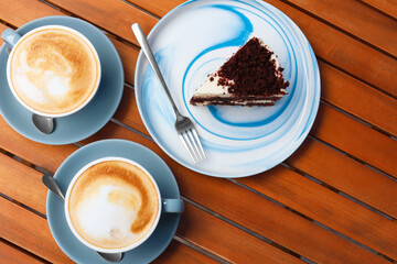 Cups of aromatic coffee and slice of cake on wooden table, flat lay