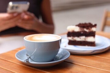 Woman with cup of coffee and cake at wooden table, selective focus