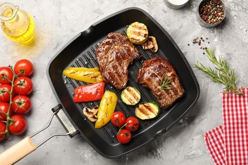 Pan with grilled beef steaks, mushrooms, vegetables and spices on grey textured table, flat lay