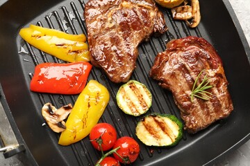 Pan with grilled beef steaks, mushrooms and vegetables on grey table, top view