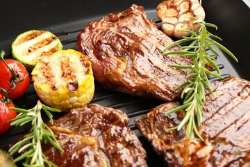 Grilled beef steaks, rosemary and vegetables on black pan, closeup