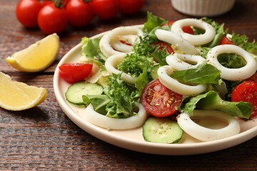 Delicious salad with squid rings, vegetables and spices served on wooden table, closeup