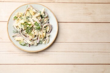 Tasty salad with squid rings, onion and eggs served on light wooden table, top view. Space for text