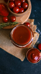 Jar of tomato sauce with fresh tomatoes and rosemary on a rustic table.