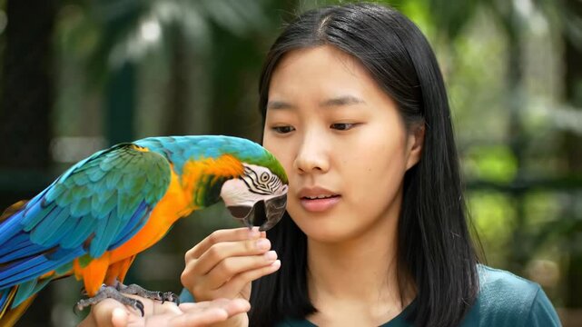 Woman interacting with colorful parrot perched on her hand outdoors