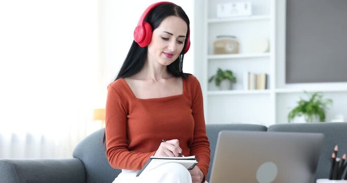 Woman taking notes while passing online test via laptop at home